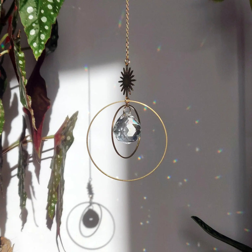 SunCatcher Attrape-soleil Étoile avec cristal de verre, anneaux en laiton et chaîne, projetant des reflets colorés dans une pièce ensoleillée.