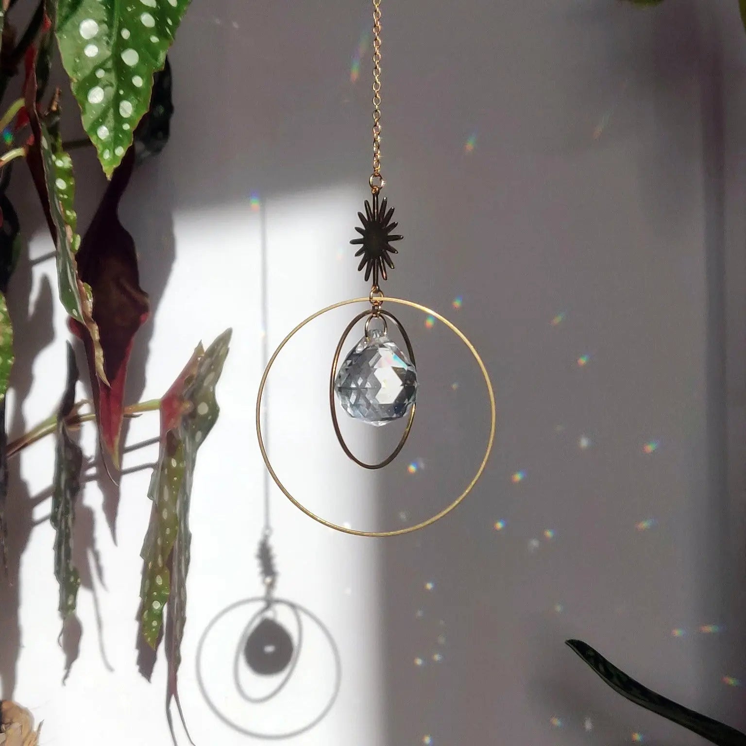 SunCatcher Attrape-soleil Étoile avec cristal de verre, anneaux en laiton et chaîne, projetant des reflets colorés dans une pièce ensoleillée.