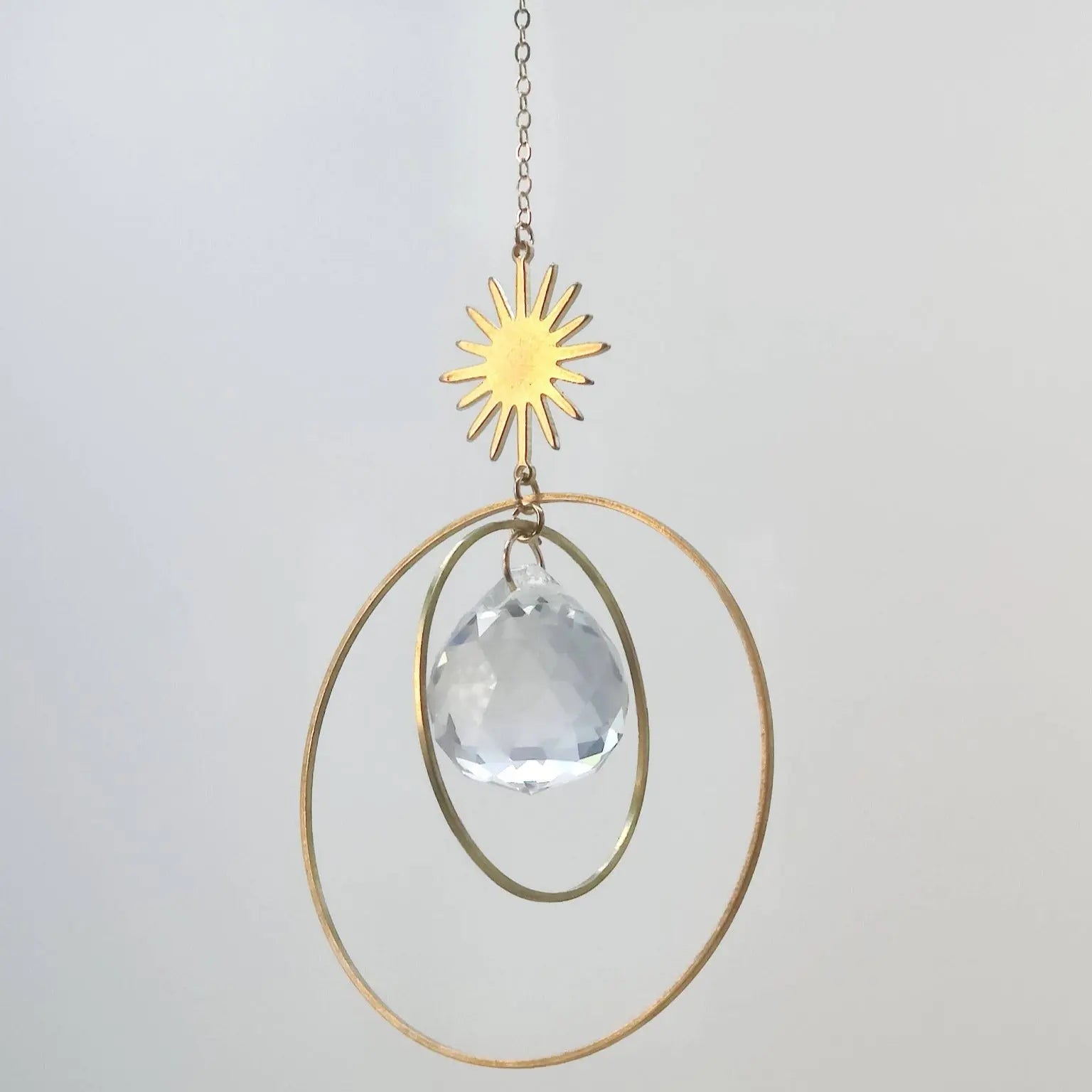 Attrape-soleil en cristal avec connecteur étoile en laiton, anneaux dorés et prisme en cristal de verre, suspendu à une chaîne délicate.