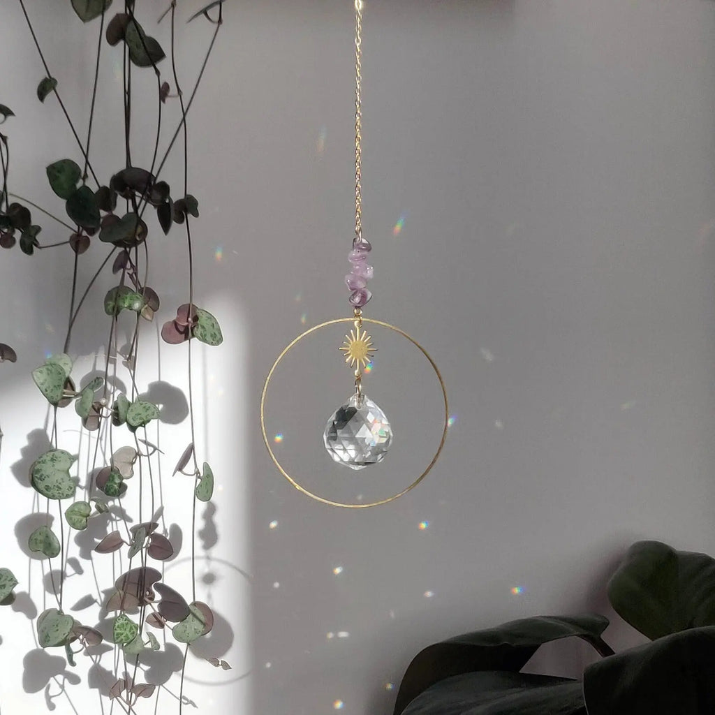 Améthyste attrape-soleil Dolce avec cristal de verre et chaîne dorée, diffusant des jeux de lumière, accroché près de plantes d'intérieur.