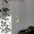 Améthyste attrape-soleil Dolce avec cristal de verre et chaîne dorée, diffusant des jeux de lumière, accroché près de plantes d'intérieur.