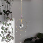 Améthyste attrape-soleil Dolce avec cristal de verre et chaîne dorée, diffusant des jeux de lumière, accroché près de plantes d'intérieur.