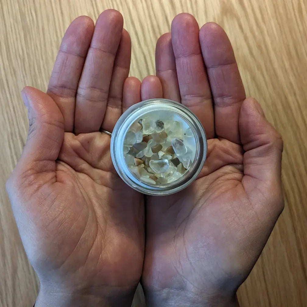 Bougie avec pierre de lithothérapie Féminin Sacré dans des mains, bocal en verre avec pierres naturelles, ambiance zen et féminité.