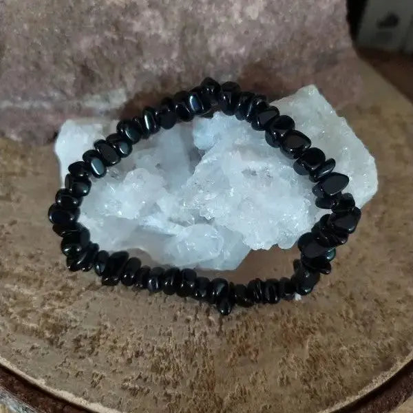 Bracelet en pierres naturelles d'osbisidienne noires exposé sur une surface de cristal et de bois.