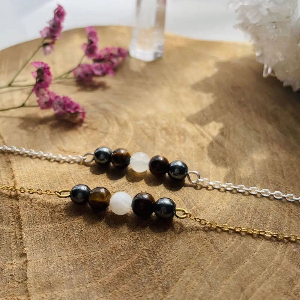 Bracelet Protection Femme Pentaperle avec pierres d’hématite, œil de tigre et pierre de lune sur fond en bois.