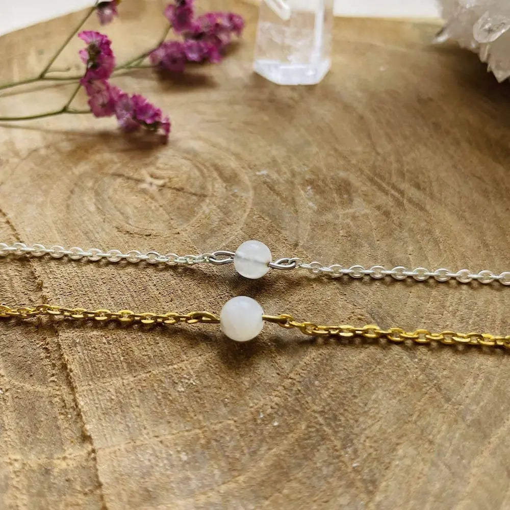 Bracelet avec Pierre de Lune en argent et or avec perles de pierre de lune sur un fond bois et fleurs séchées.