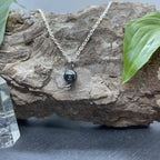 Collier en hématite noire pour femme, en pendentif sur une chaîne en argent, reposant sur une pierre naturelle.