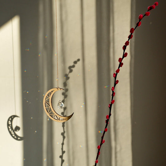 Attrape-soleil en forme de lune, projetant des reflets et des ombres colorés, à côté d'un vase aux branches rouges.