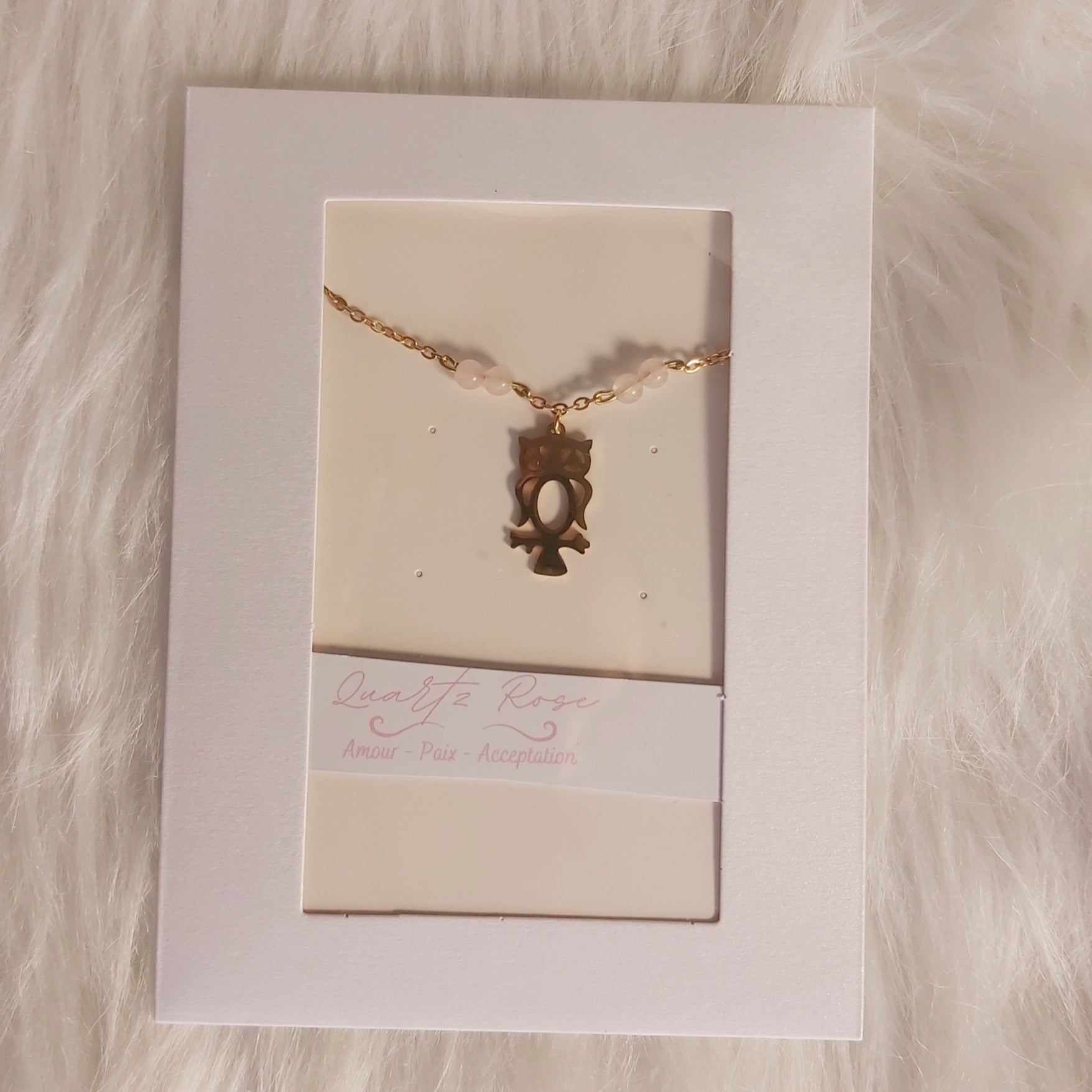 Bracelet Charme hibou doré sur fond de carte blanche avec texture de fourrure douce.