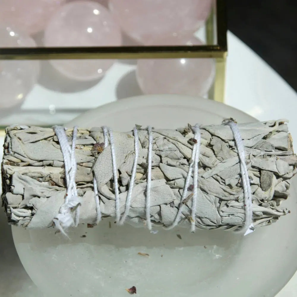 baton de sauge pour purifier de Californie sur un plat en verre, entouré de cristaux roses, utilisé pour la purification et le nettoyage énergétique.
