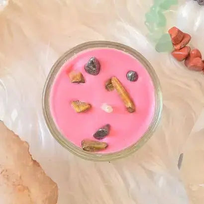 Bougie chakra racine rose avec cristaux naturels, entourée de pierres lithothérapie sur un fond doux.