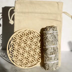 Kit de purification avec bâton de sauge blanche et fleur de vie en bois pour recharger les pierres, sac en toile en arrière-plan.