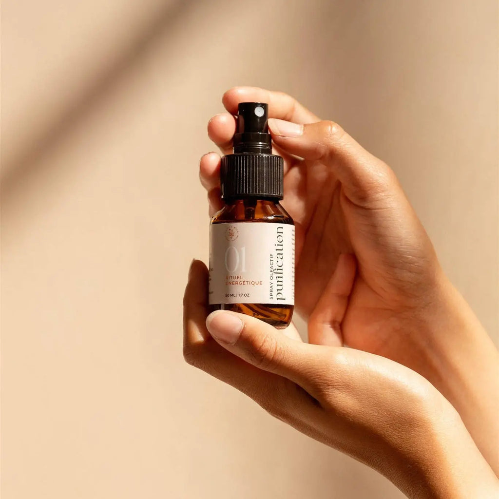 Spray aux huiles essentielles bio pour purification en aromathérapie, tenu dans les mains avec un fond neutre.