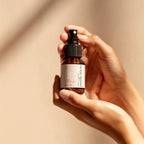 Spray aux huiles essentielles bio pour purification en aromathérapie, tenu dans les mains avec un fond neutre.